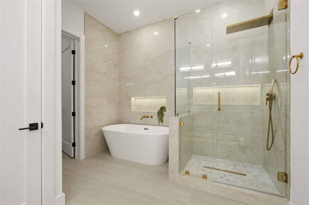 Freestanding soaking tub, walk-in shower with glass enclosure, gold-finish fixtures, and light-toned tile flooring