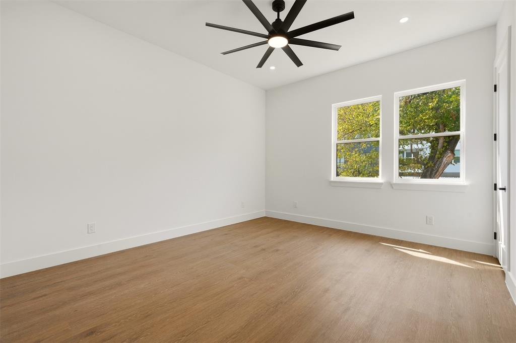 Spacious room featuring wood-finish flooring, two large windows, a modern ceiling fan, and recessed lighting