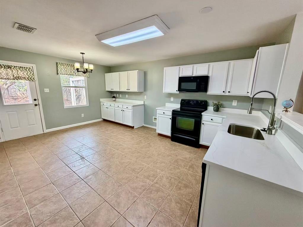 White cabinetry with black hardware, black appliances, light-toned tile flooring, and light-toned countertops