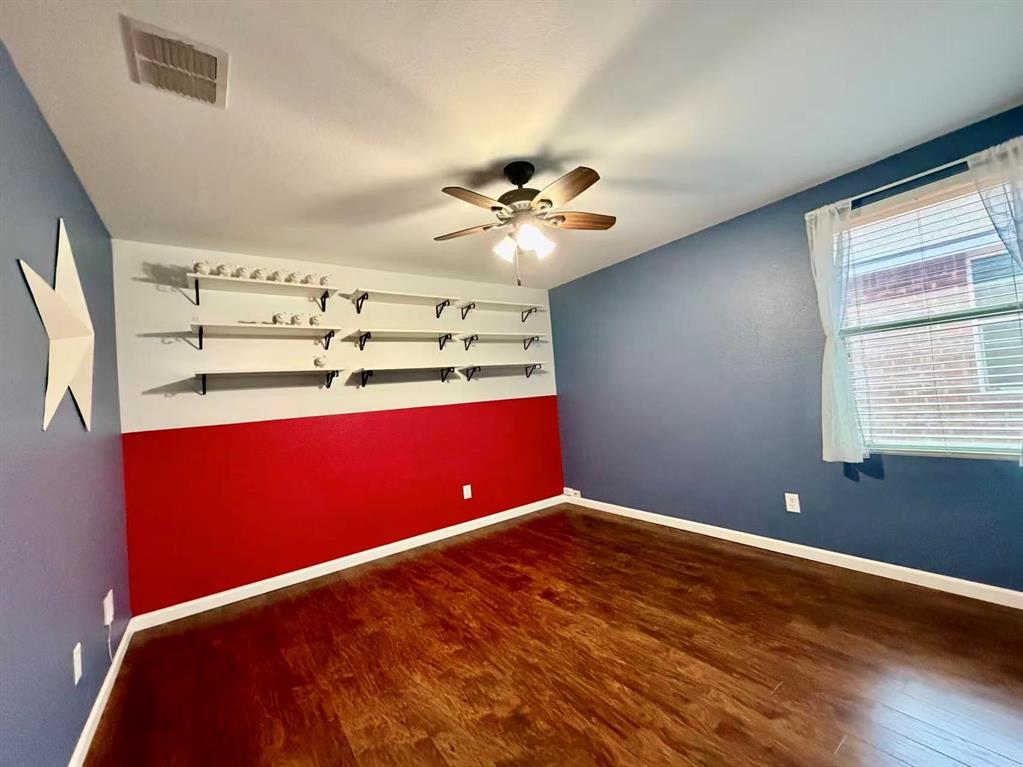 Wood-finish flooring, ceiling fan with integrated lighting, window with blinds, and built-in shelving