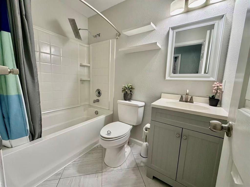 Bathroom featuring a white bathtub, tiled shower surround, light-colored vanity with an integrated sink, and a framed mirror