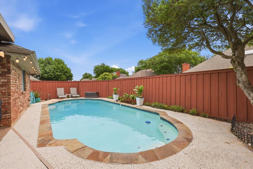Private backyard featuring a swimming pool with stone coping, textured concrete patio, and a high wood fence