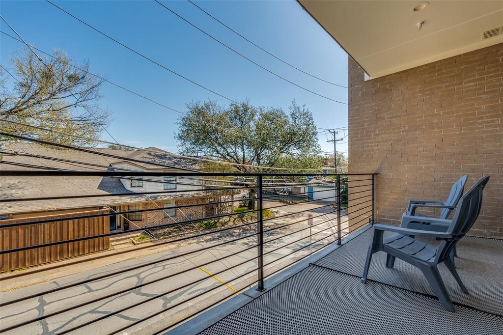 Balcony with black metal horizontal railing and overhead lighting, featuring a brick exterior wall and textured outdoor flooring