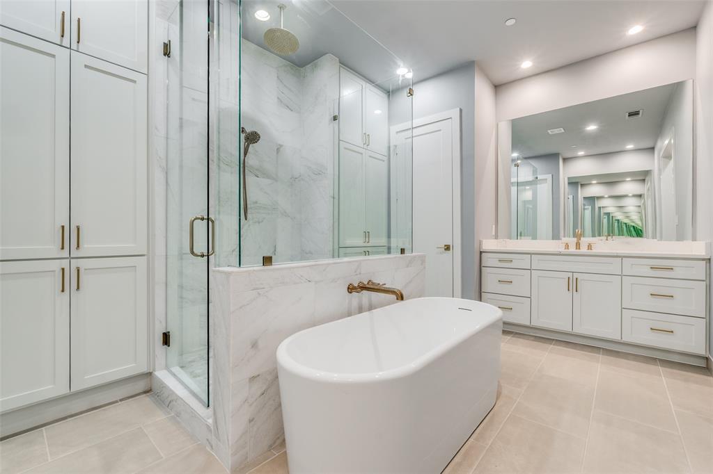 Freestanding soaking tub, glass-enclosed shower with a rain showerhead, double vanity with an integrated mirror, and extensive built-in cabinetry