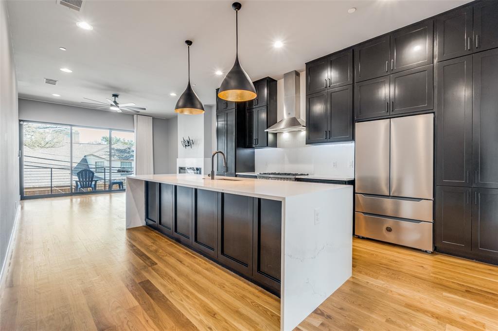 Modern kitchen featuring dark cabinetry, stainless steel appliances, a large center island with a white countertop, and wood-finish flooring