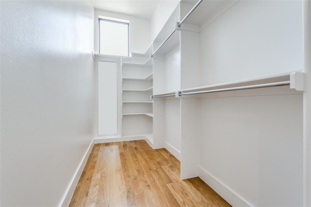 Spacious walk-in closet featuring wood-finish flooring, built-in shelving, and hanging rods
