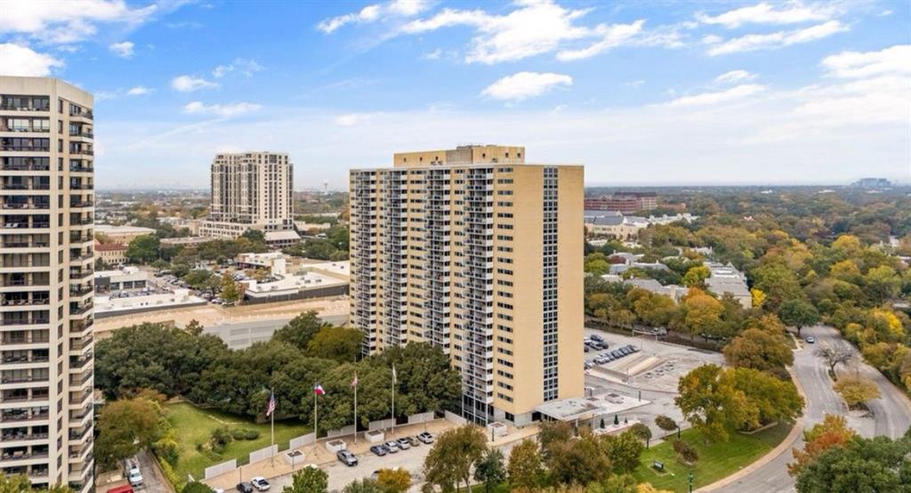 High-rise residential building with multiple balconies, surrounded by mature trees and manicured green spaces