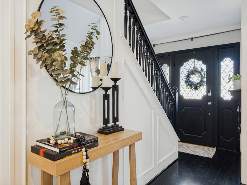 Foyer entry featuring black-painted solid wood door with diamond-pattern glass sidelights, dark-stained wood-finish flooring, and wall panel molding Foyer entry featuring black-painted solid wood door with diamond-pattern glass sidelights, dark-stained wood-finish flooring, and wall panel molding