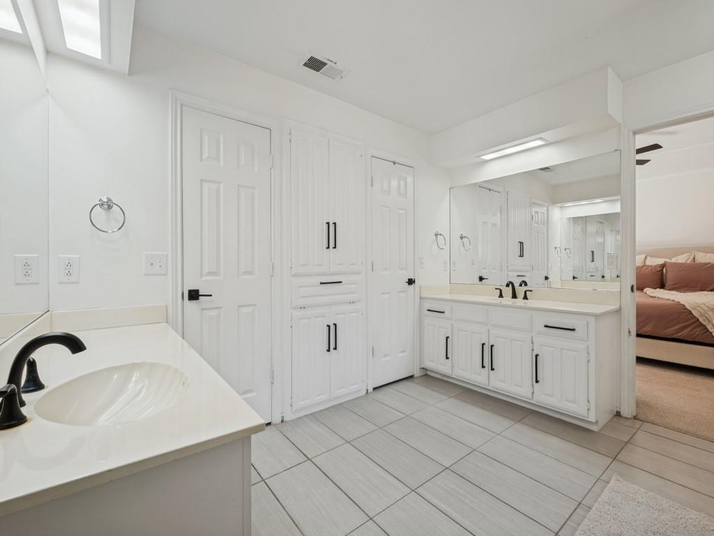 Dual-vanity bathroom featuring white cabinetry with matte black hardware, integrated countertops with undermount sinks, large-scale mirrors, and tile flooring
