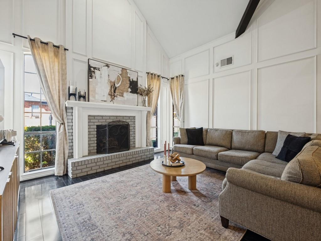 Vaulted ceilings with board-and-batten wall detailing, floor-to-ceiling windows, and a brick fireplace featuring a wood mantelpiece and hearth Vaulted ceilings with board-and-batten wall detailing, floor-to-ceiling windows, and a brick fireplace featuring a wood mantelpiece and hearth