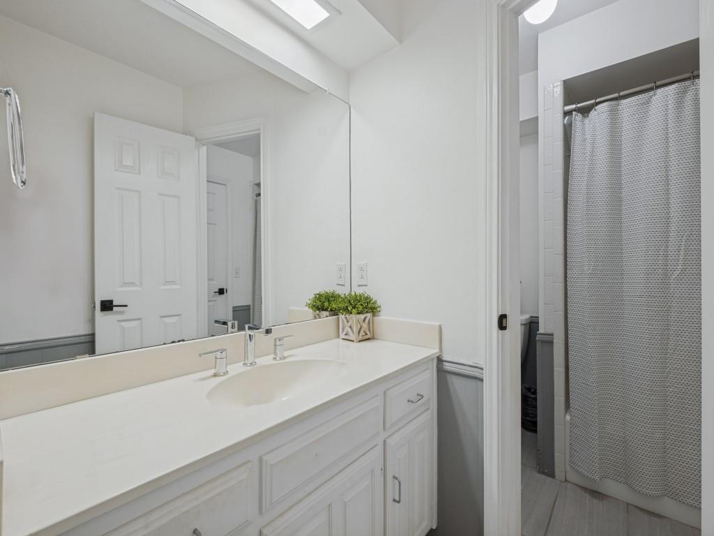 Bathroom vanity featuring a white countertop with an integrated basin, chrome widespread faucet, full-width mirror, and white shaker-style cabinetry