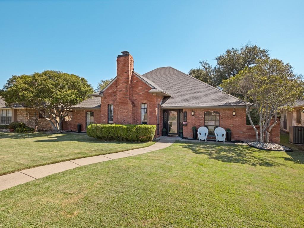 Traditional brick exterior featuring an arched entryway, prominent masonry chimney, and manicured lawn