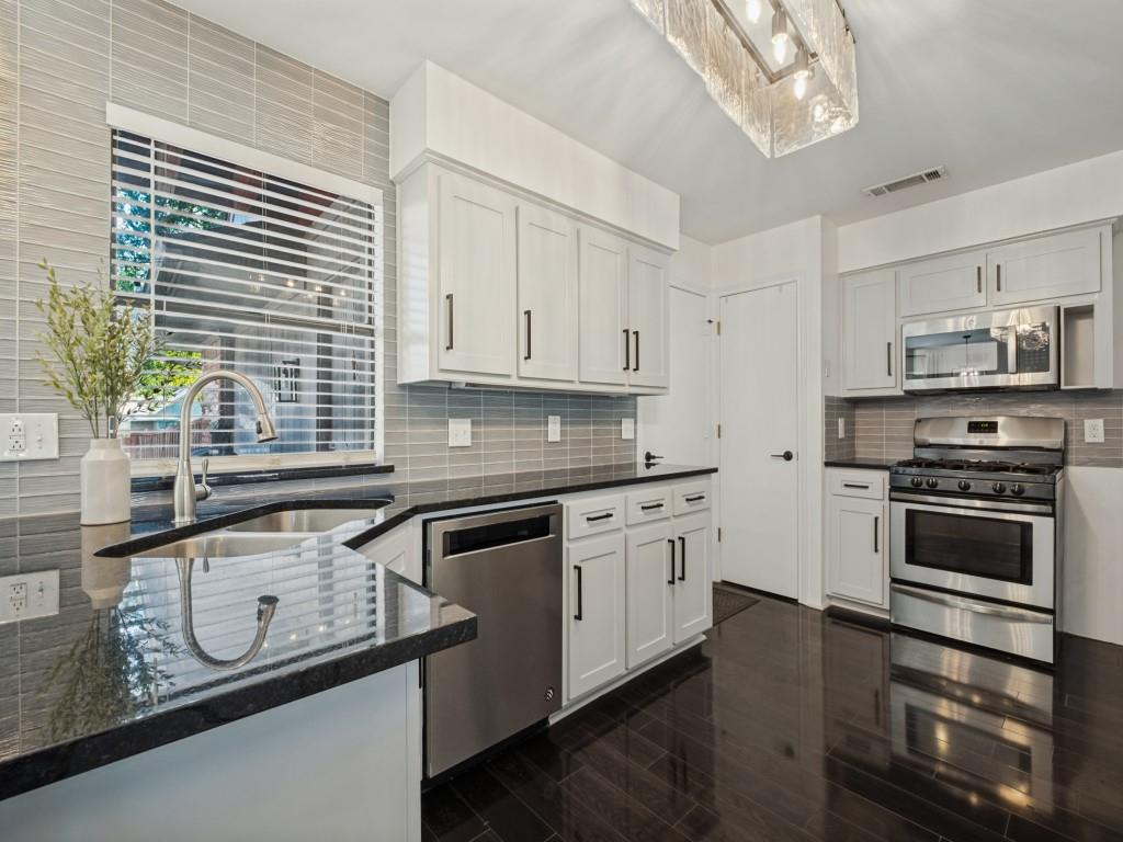 Kitchen featuring white shaker-style cabinetry, dark stone countertops, stainless steel appliances, linear tile backsplash, and wood-finish flooring