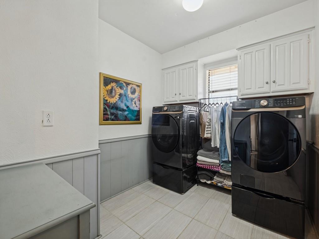 Laundry space featuring tile flooring, white upper wall cabinetry, and gray lower wall wainscoting