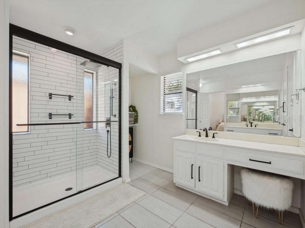 Bathroom featuring a glass-enclosed shower with horizontal wall tile, white cabinetry, dual-faucet vanity with integrated knee space, and large-format tile flooring