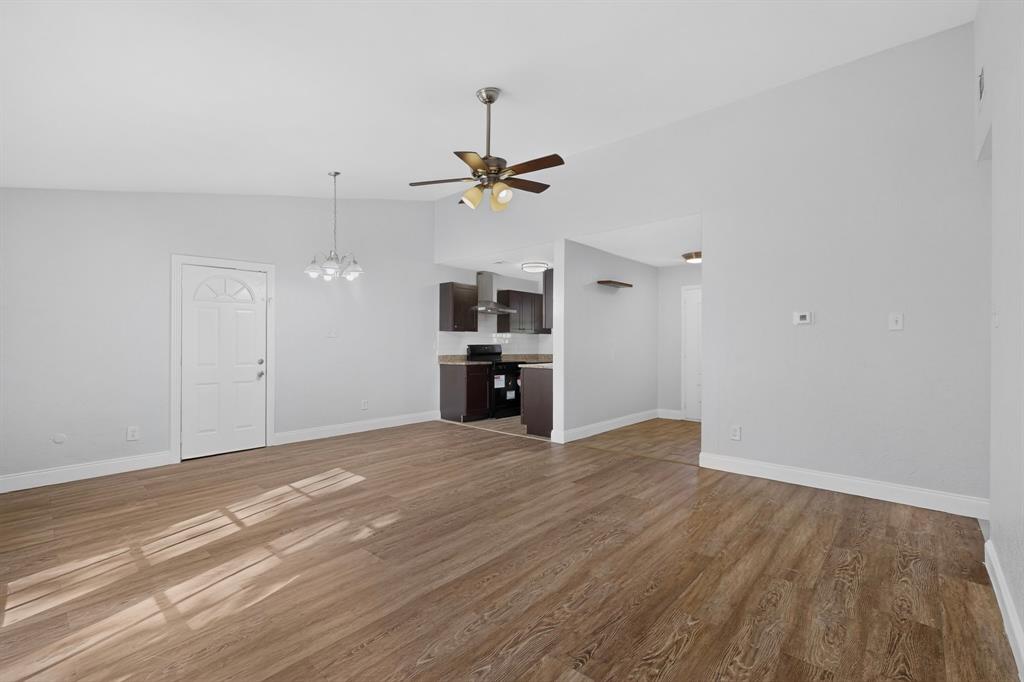 Open-concept area featuring vaulted ceilings, wood-finish flooring, a ceiling fan with integrated lighting, and a multi-pendant light fixture Open-concept area featuring vaulted ceilings, wood-finish flooring, a ceiling fan with integrated lighting, and a multi-pendant light fixture