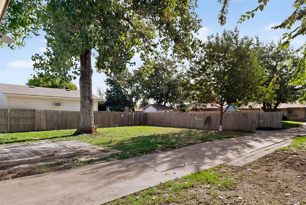 Expansive backyard featuring a concrete patio, wood-slat perimeter fencing, and mature trees