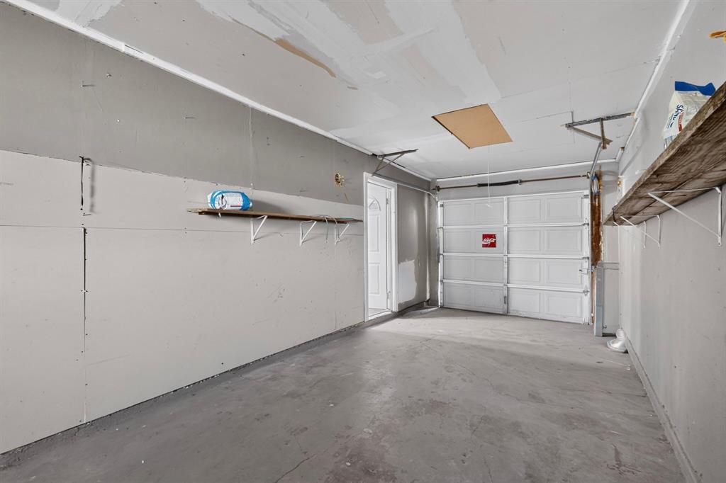 Enclosed garage space featuring a paneled sectional door, concrete flooring, built-in wall shelving, and an integrated ceiling access panel