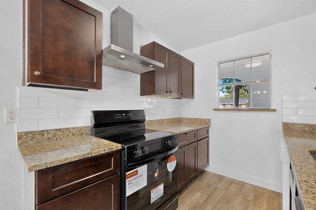 Kitchen featuring dark wood cabinetry, stone countertops, white subway tile backsplash, stainless steel range hood, and wood-finish flooring Kitchen featuring dark wood cabinetry, stone countertops, white subway tile backsplash, stainless steel range hood, and wood-finish flooring