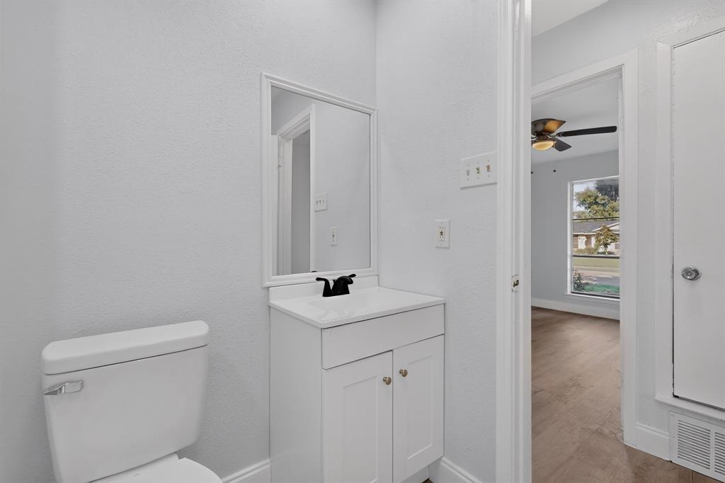 White vanity cabinet with a rectangular countertop, framed mirror, matte black faucet, and white toilet