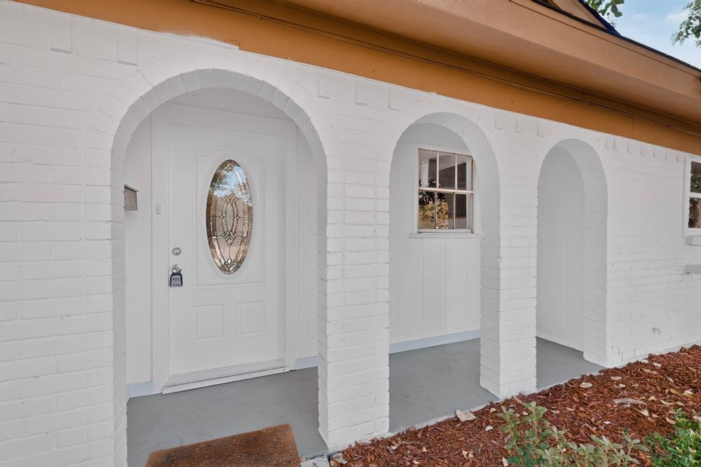 Painted brick facade with arched architectural entry, covered porch, and exterior door featuring an oval glass inlay