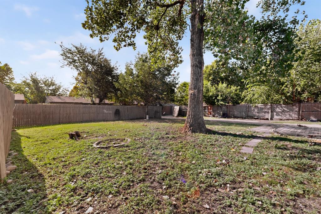 Spacious backyard featuring a perimeter wood fence, mature tree, and stone paver area