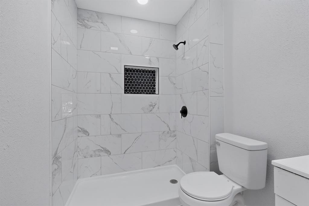 Walk-in shower featuring large-format stone-patterned tile, matte black shower fixtures, and a recessed hexagonal tile niche