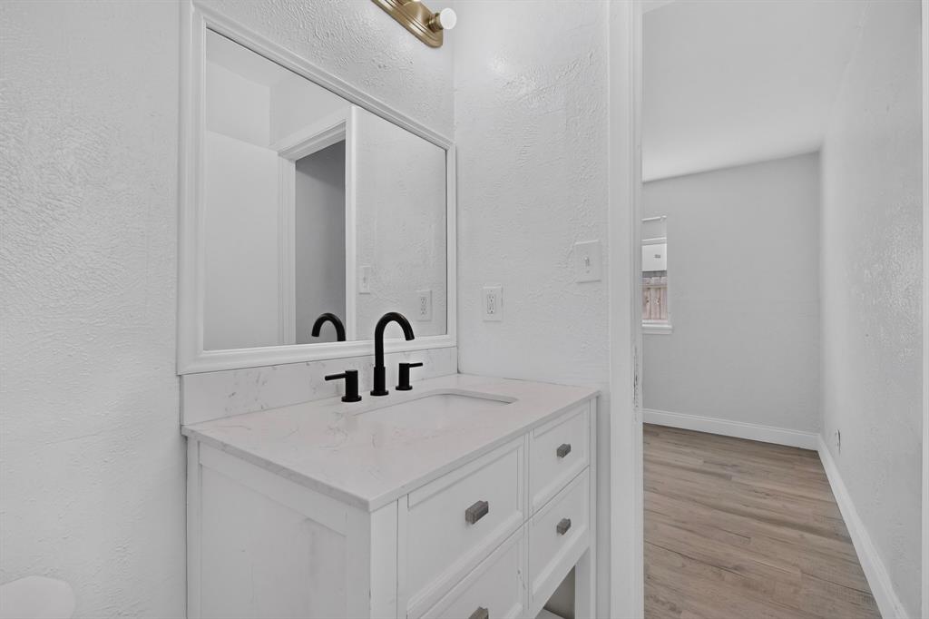 White vanity with a stone-finish countertop, integrated basin, matte black faucet, framed mirror, and warm-toned vanity lighting