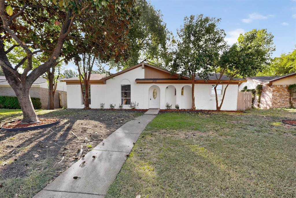 Single-story exterior featuring a light-colored stucco facade, decorative arched entryway, and mature trees