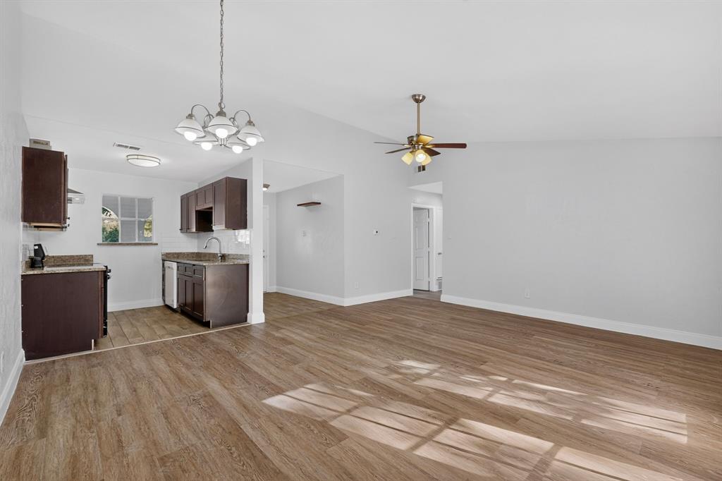 Open-concept area featuring wood-finish flooring, dark cabinetry, stone-surface countertops, a multi-bulb chandelier, and a ceiling fan Open-concept area featuring wood-finish flooring, dark cabinetry, stone-surface countertops, a multi-bulb chandelier, and a ceiling fan