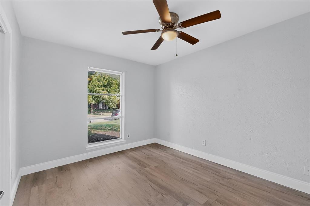 Bedroom featuring wood-finish flooring, light-toned wall finishes, a multi-pane window, and a ceiling-mounted fan with integrated lighting