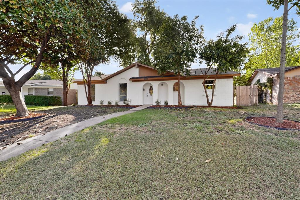 Single-story residence featuring a painted brick exterior, arched entryway, concrete walkway, and mature landscaping