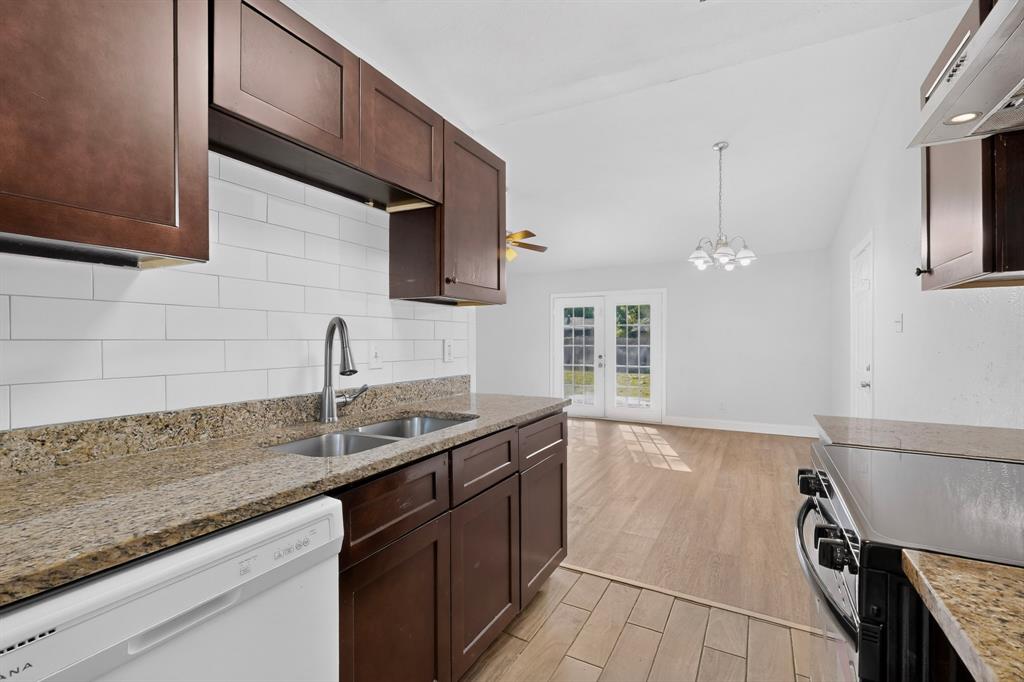 Kitchen featuring dark-toned cabinetry, stone-finish countertops, subway tile backsplash, stainless steel faucet, and wood-finish tile flooring