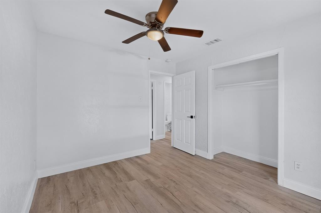 Primary bedroom featuring wood-finish flooring, a ceiling fan with integrated lighting, a walk-in closet, and a white six-panel interior door with matte black hardware