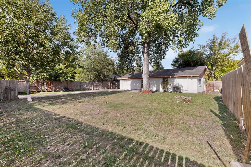 Expansive backyard featuring a large grass lawn, mature trees, and wooden perimeter fencing