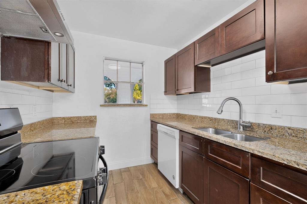 Kitchen featuring dark wood-finish cabinetry, stone countertops, white subway tile backsplash, stainless steel dual-basin sink with pull-down faucet, and wood-finish flooring