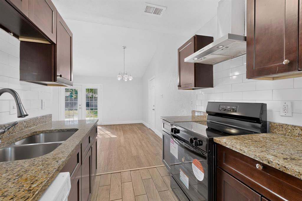 Kitchen featuring wood-finish cabinetry, stone countertops, a white subway tile backsplash, stainless steel sink with a high-arch faucet, and wood-finish tile flooring Kitchen featuring wood-finish cabinetry, stone countertops, a white subway tile backsplash, stainless steel sink with a high-arch faucet, and wood-finish tile flooring