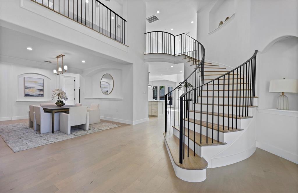 Curved staircase with black iron balusters, high ceilings, wood-finish flooring, recessed lighting, and a dining area with a chandelier Curved staircase with black iron balusters, high ceilings, wood-finish flooring, recessed lighting, and a dining area with a chandelier