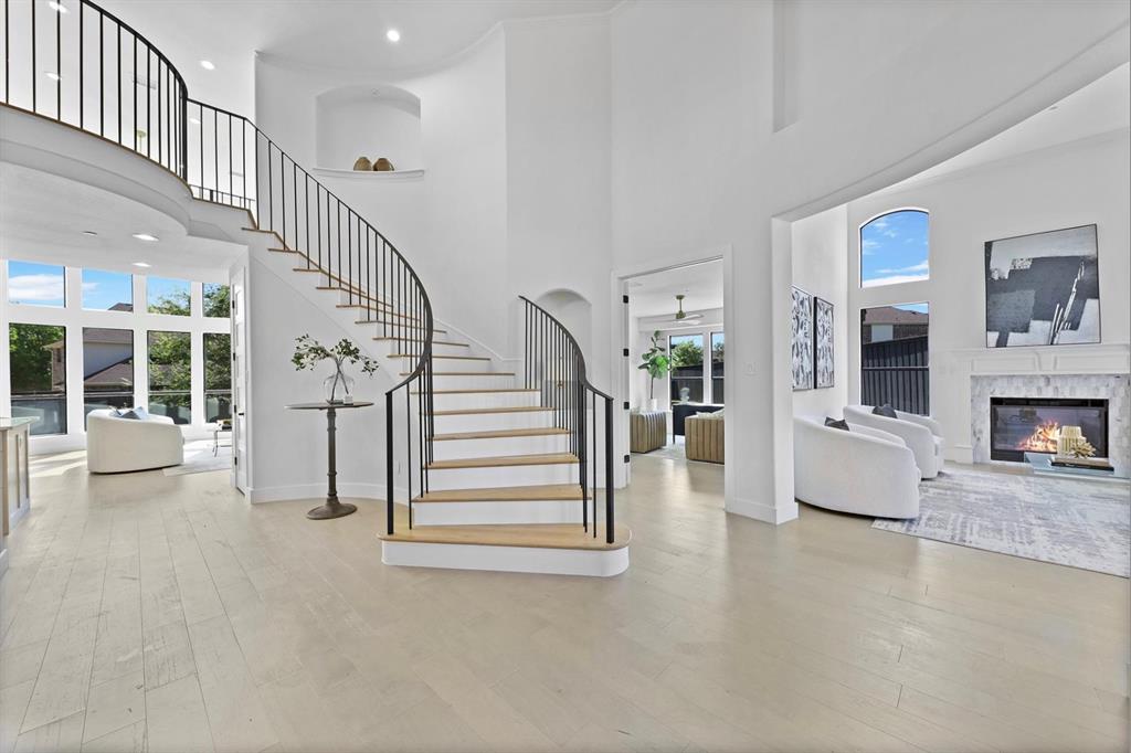 Grand curved staircase with wrought iron balusters, high ceilings, large arched windows, wood-finish flooring, and a fireplace with a decorative mantel Grand curved staircase with wrought iron balusters, high ceilings, large arched windows, wood-finish flooring, and a fireplace with a decorative mantel