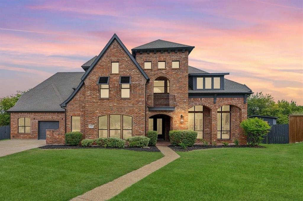 Brick exterior with dark gray roofing, an integrated garage, a second-story balcony, and arched window details Brick exterior with dark gray roofing, an integrated garage, a second-story balcony, and arched window details