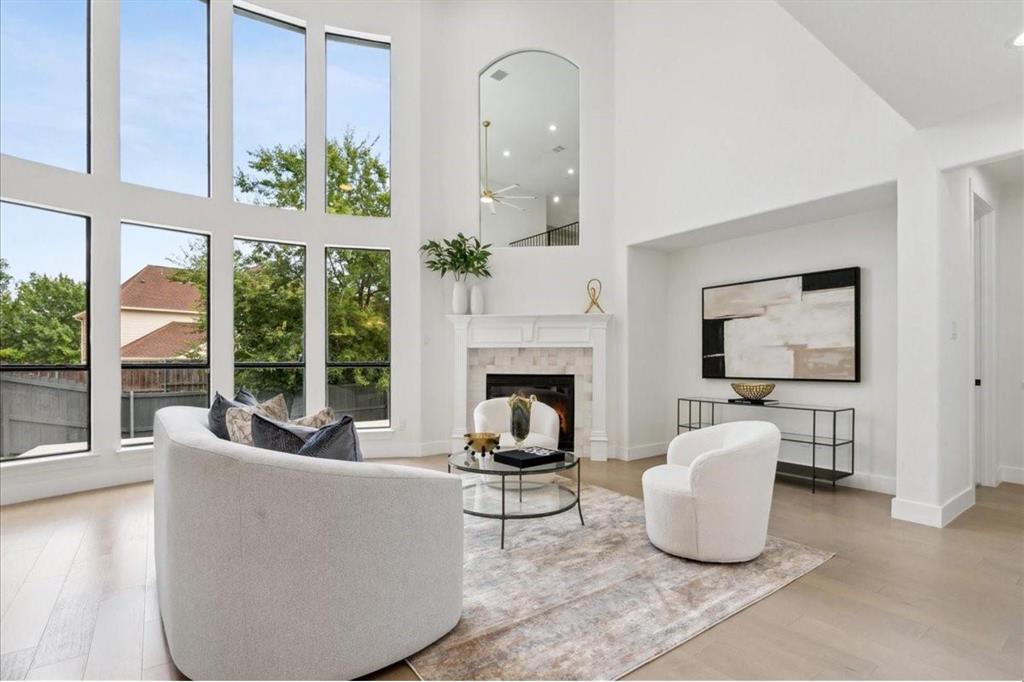 Soaring ceilings, expansive window wall, light wood-finish flooring, fireplace with stone surround, and a white mantel Soaring ceilings, expansive window wall, light wood-finish flooring, fireplace with stone surround, and a white mantel