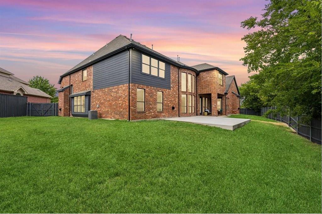 Expansive green lawn with a concrete patio, brick exterior with dark siding, and large windows