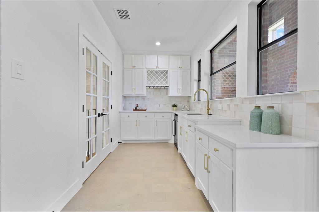 Full kitchen featuring white cabinetry, light-toned countertops, a built-in wine rack, and a gold-finish faucet