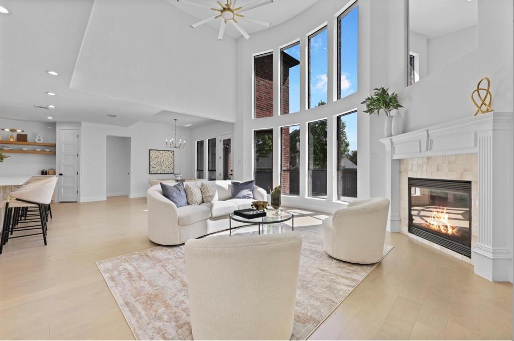 Double-height ceiling, floor-to-ceiling windows, wood-finish flooring, built-in fireplace with stone surround, and a ceiling fan with integrated lighting Double-height ceiling, floor-to-ceiling windows, wood-finish flooring, built-in fireplace with stone surround, and a ceiling fan with integrated lighting