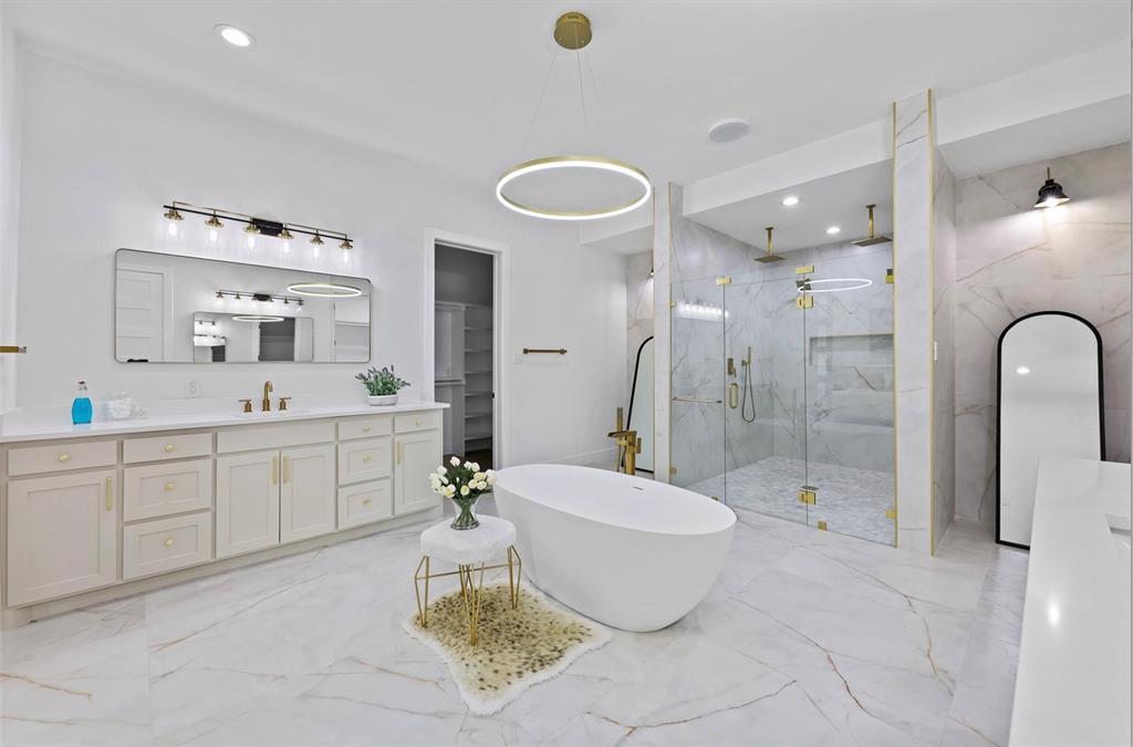Spacious bathroom featuring a freestanding soaking tub, dual vanity with undermount sinks, glass-enclosed shower with multiple shower heads, and large format marble-look tile flooring