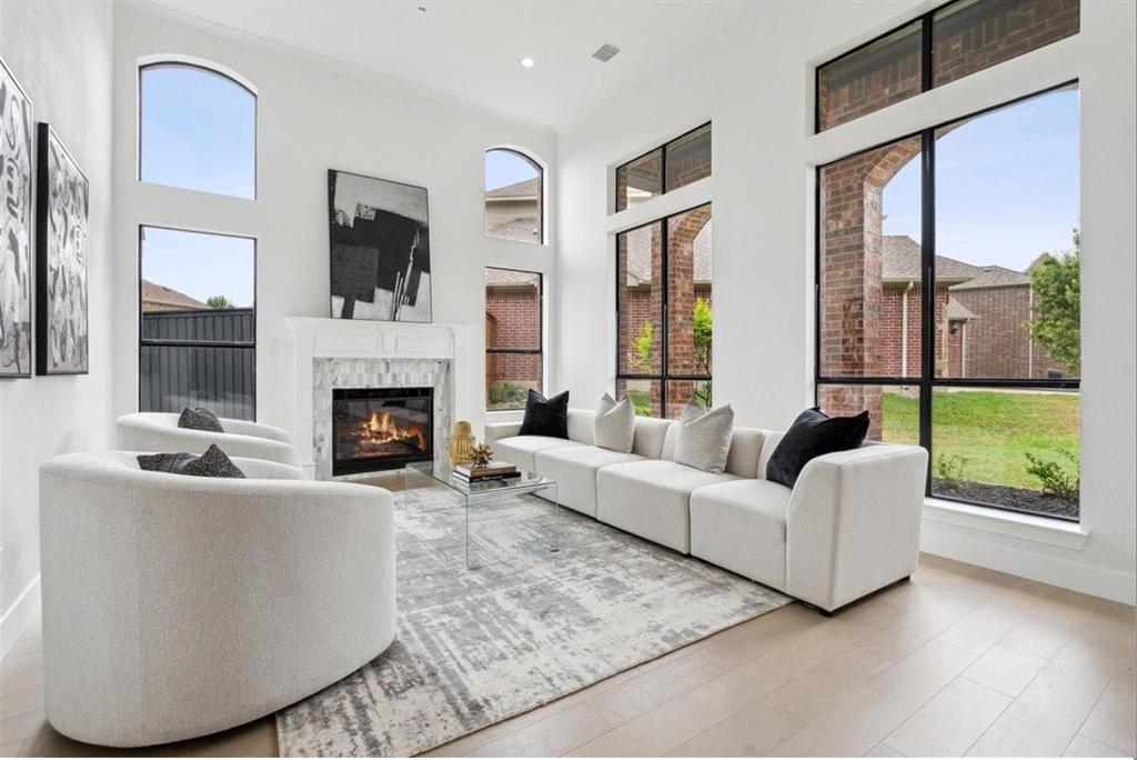 Living space with high ceilings, a fireplace featuring a stone surround, wood-finish flooring, and expansive windows