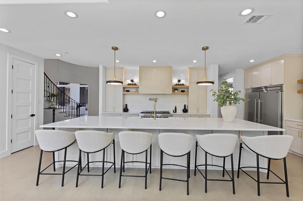 Spacious kitchen island with a white countertop, recessed lighting, stainless steel refrigerator, and gold-tone kitchen fixtures Spacious kitchen island with a white countertop, recessed lighting, stainless steel refrigerator, and gold-tone kitchen fixtures