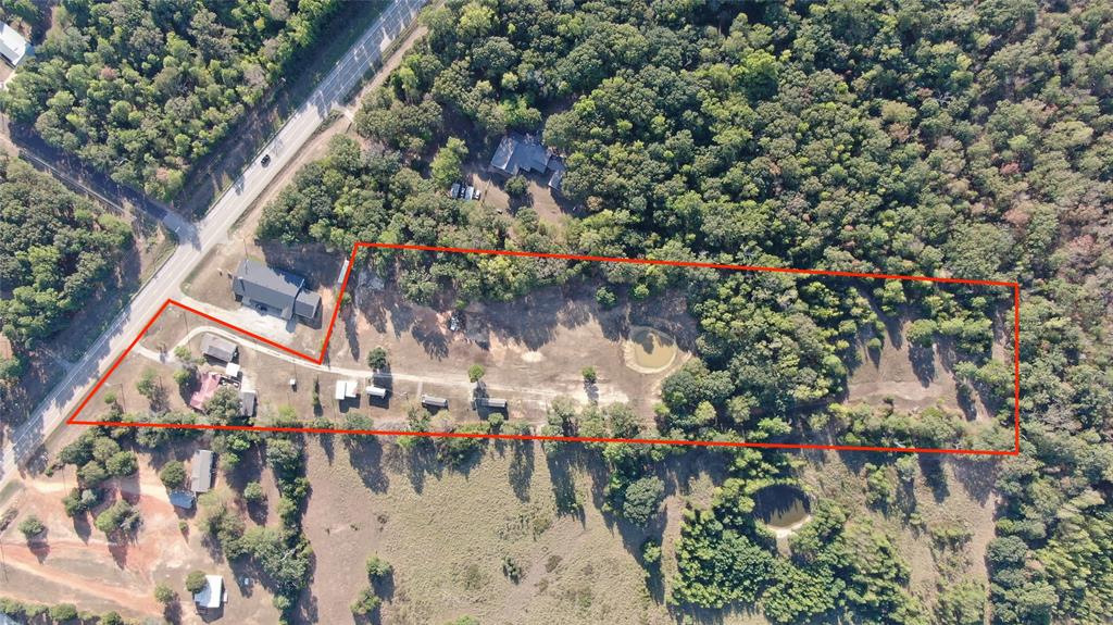 Extensive acreage featuring natural tree coverage, multiple structures, and a prominent roadway frontage