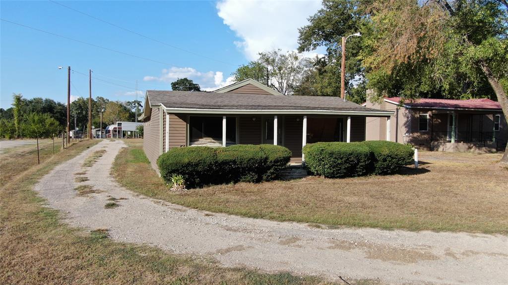 Siding exterior with covered porch, gravel driveway, and mature landscaping