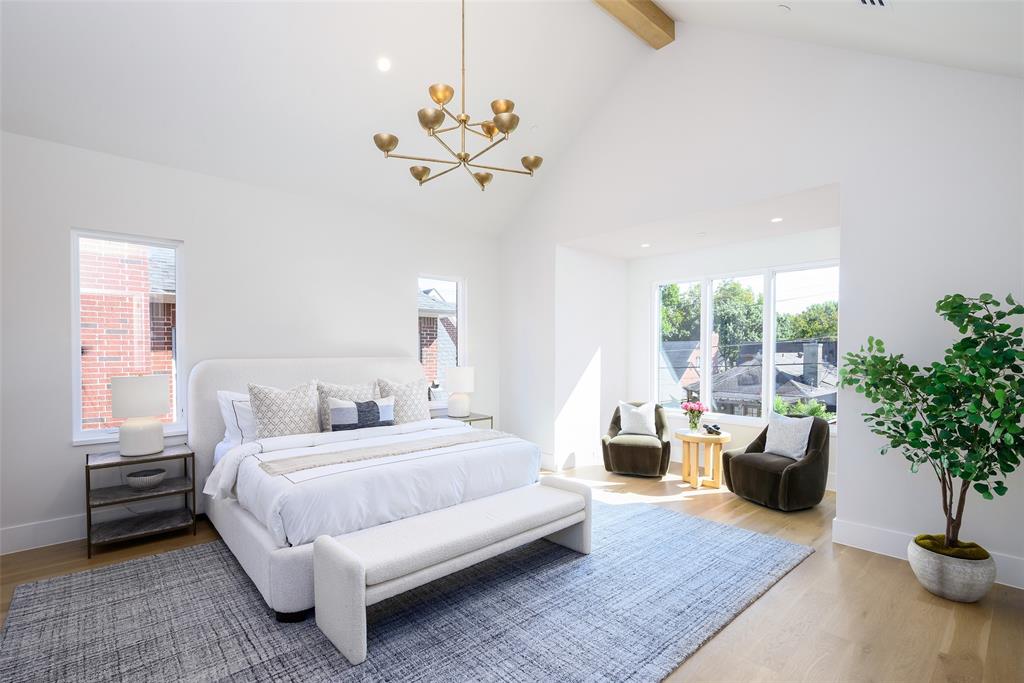 Spacious primary suite with vaulted ceiling and white oak ceiling beams, sitting area and windows overlooking backyard